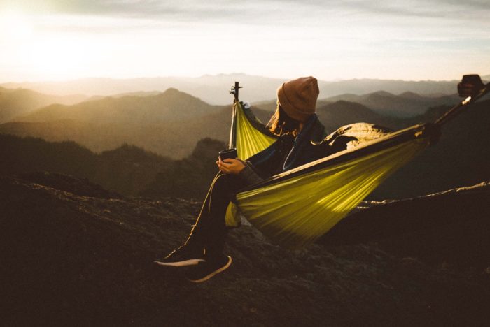 unrecognizable woman sitting in hammock above mountains